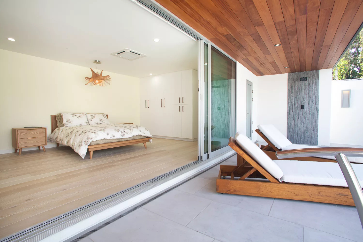 Poolside room with custom glass sliding doors opening up to lounge chairs next to the pool and an outdoor shower.